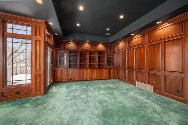 carpeted spare room featuring built in features, wood walls, and a raised ceiling