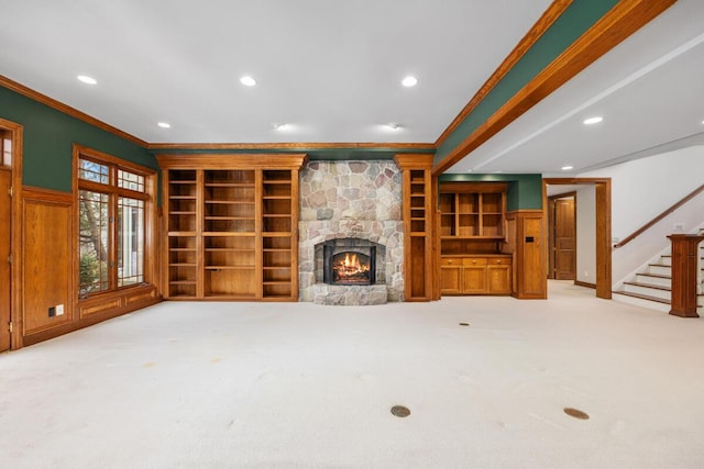 unfurnished living room with a fireplace, built in shelves, crown molding, and light colored carpet