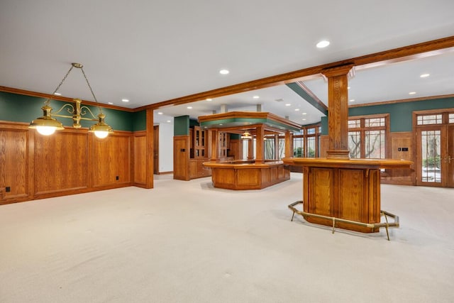 kitchen featuring a breakfast bar area, decorative light fixtures, crown molding, light carpet, and decorative columns