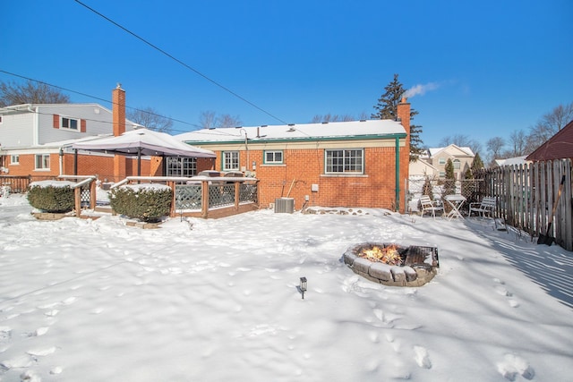 snow covered house featuring an outdoor fire pit, cooling unit, fence private yard, brick siding, and a gazebo