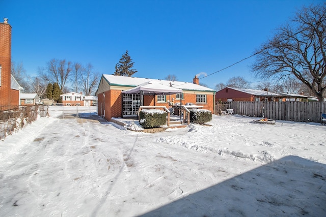 snow covered house featuring brick siding, a chimney, and fence