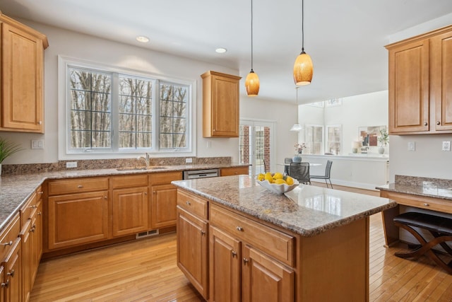 kitchen featuring light wood-type flooring, light stone counters, pendant lighting, a center island, and sink