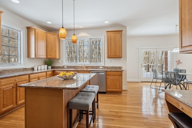 kitchen featuring dishwasher, light stone countertops, decorative light fixtures, a center island, and light wood-type flooring