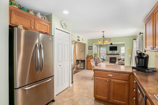 kitchen with appliances with stainless steel finishes, light tile patterned flooring, pendant lighting, a chandelier, and a fireplace