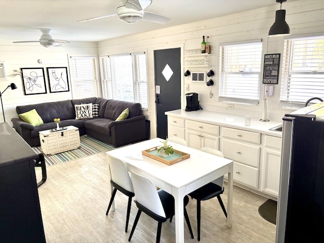 dining area featuring light wood-style floors, ceiling fan, and wood walls
