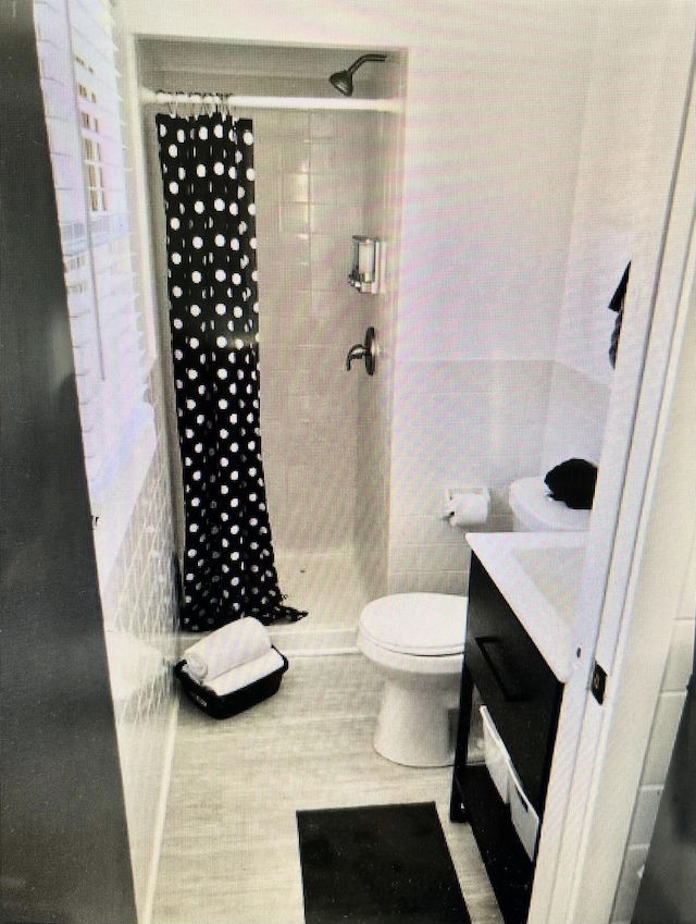 full bathroom with tile walls, tiled shower, vanity, and toilet
