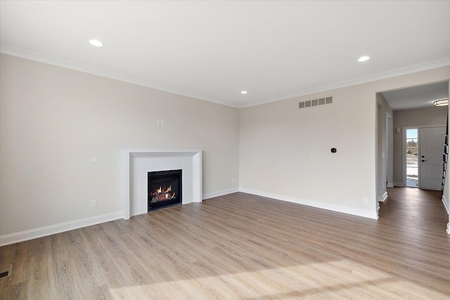 unfurnished living room with a warm lit fireplace, visible vents, light wood-style flooring, and baseboards