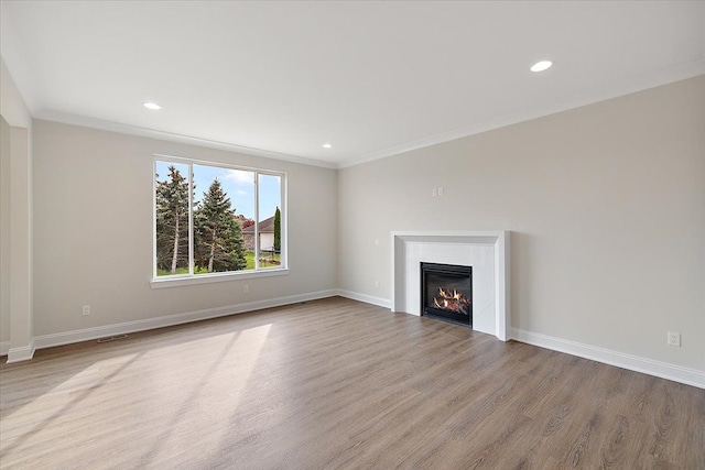 unfurnished living room featuring baseboards, a glass covered fireplace, ornamental molding, light wood-type flooring, and recessed lighting