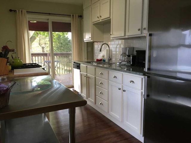 kitchen with appliances with stainless steel finishes, dark stone counters, decorative backsplash, white cabinetry, and dark hardwood / wood-style floors