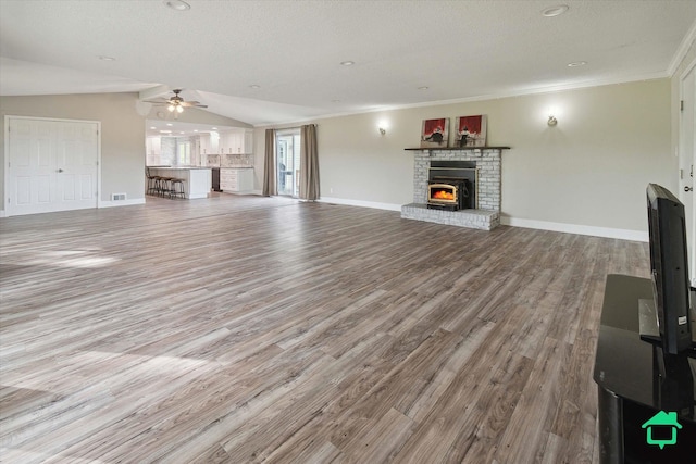 unfurnished living room featuring a fireplace, baseboards, vaulted ceiling, ornamental molding, and light wood-type flooring