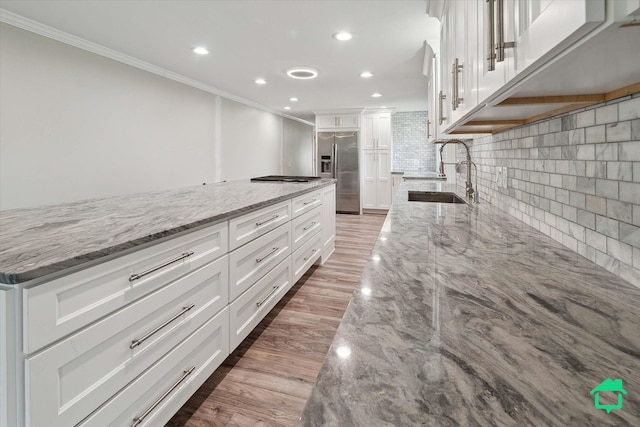 kitchen featuring light stone counters, ornamental molding, white cabinetry, a sink, and stainless steel fridge