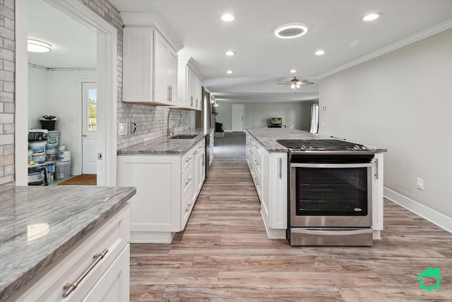 kitchen with stainless steel gas stove, light stone counters, a sink, and white cabinets