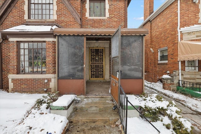 snow covered property entrance featuring brick siding