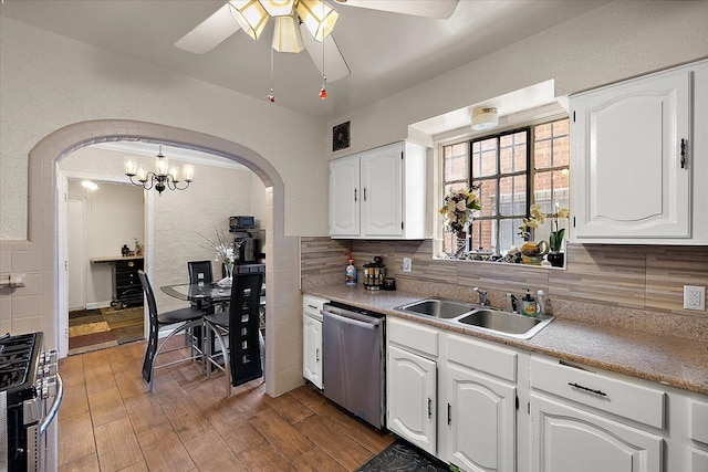 kitchen with light countertops, stainless steel appliances, a sink, arched walkways, and white cabinetry