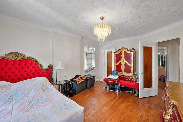 bedroom with ornamental molding, a textured ceiling, a chandelier, and wood finished floors