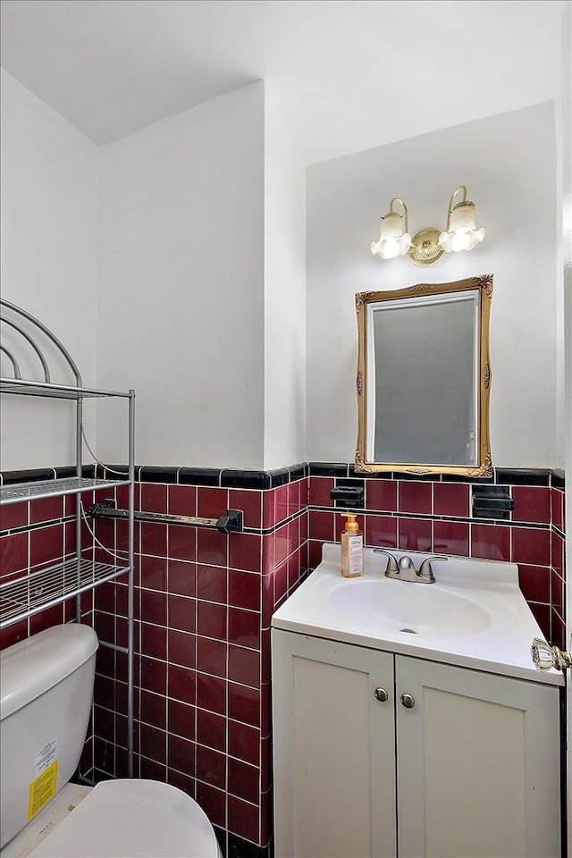 half bathroom featuring wainscoting, vanity, tile walls, and toilet