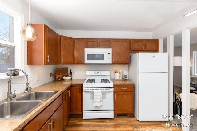 kitchen featuring white appliances, sink, backsplash, light wood-type flooring, and hanging light fixtures