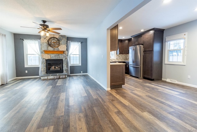 kitchen with a healthy amount of sunlight, a stone fireplace, stainless steel refrigerator, and dark brown cabinetry