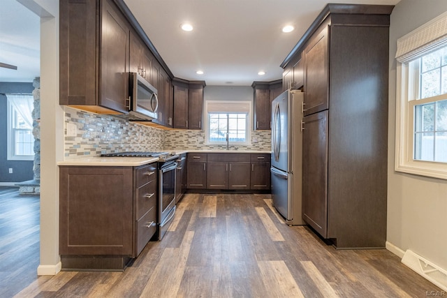 kitchen featuring appliances with stainless steel finishes, sink, dark hardwood / wood-style flooring, dark brown cabinets, and decorative backsplash