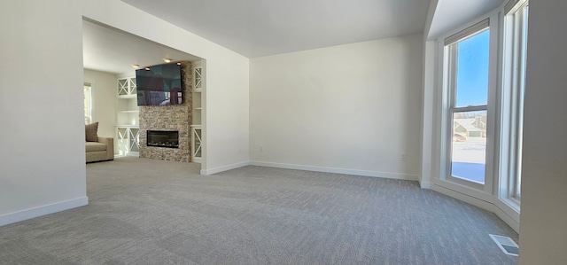 unfurnished living room with light carpet, a healthy amount of sunlight, a stone fireplace, and built in features