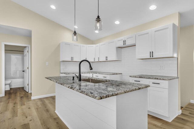 10781 Woodbrook Dr, Cement City, MI 49233 - kitchen featuring light stone counters, an island with sink, white cabinets, hanging light fixtures, and lofted ceiling