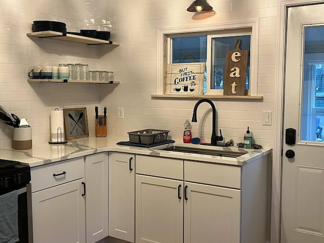 kitchen featuring stainless steel stove, sink, backsplash, light stone counters, and white cabinets