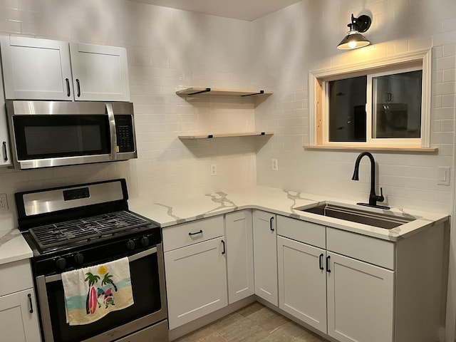 kitchen featuring sink, white cabinets, stainless steel appliances, and light stone counters