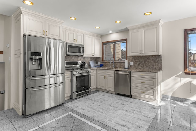 kitchen with appliances with stainless steel finishes, decorative backsplash, sink, white cabinetry, and dark stone countertops