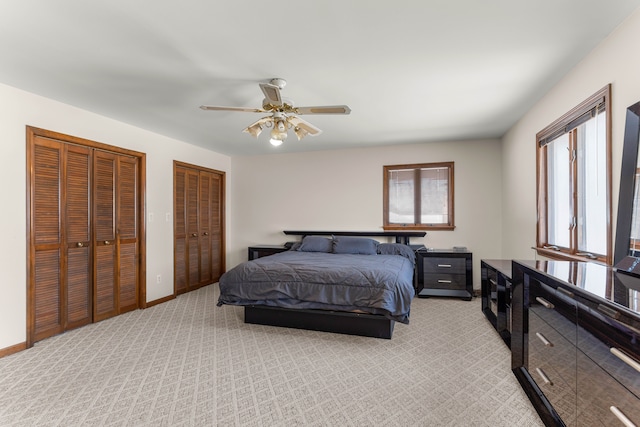 bedroom featuring light carpet, ceiling fan, and multiple closets