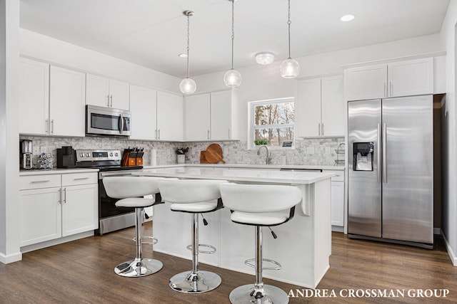 kitchen featuring appliances with stainless steel finishes, decorative light fixtures, white cabinets, and a center island