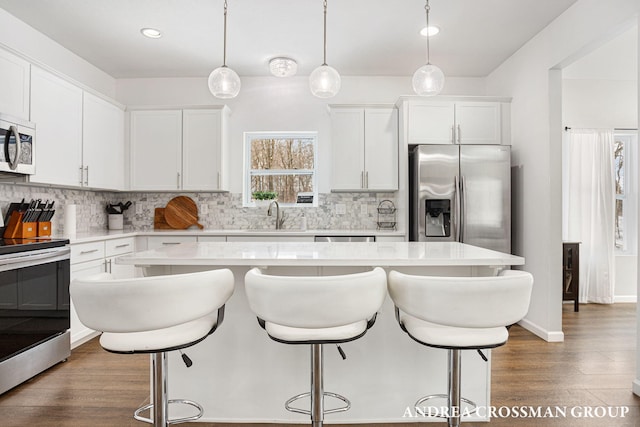 kitchen with appliances with stainless steel finishes, white cabinets, hanging light fixtures, and a center island