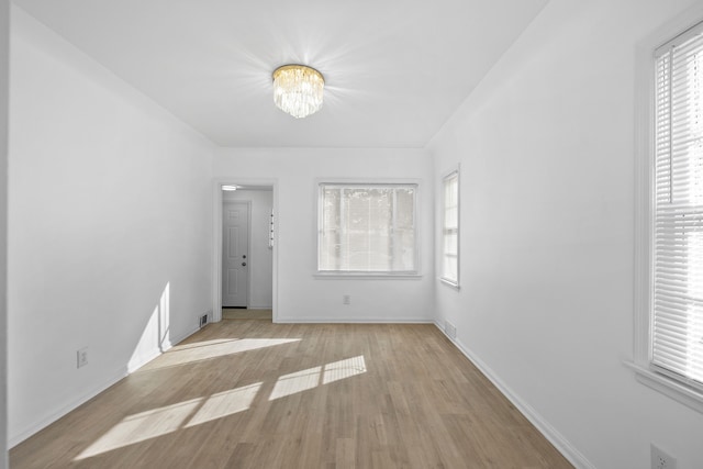 spare room featuring light hardwood / wood-style floors, a notable chandelier, and a healthy amount of sunlight