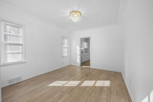 spare room with light wood-type flooring, sink, and an inviting chandelier