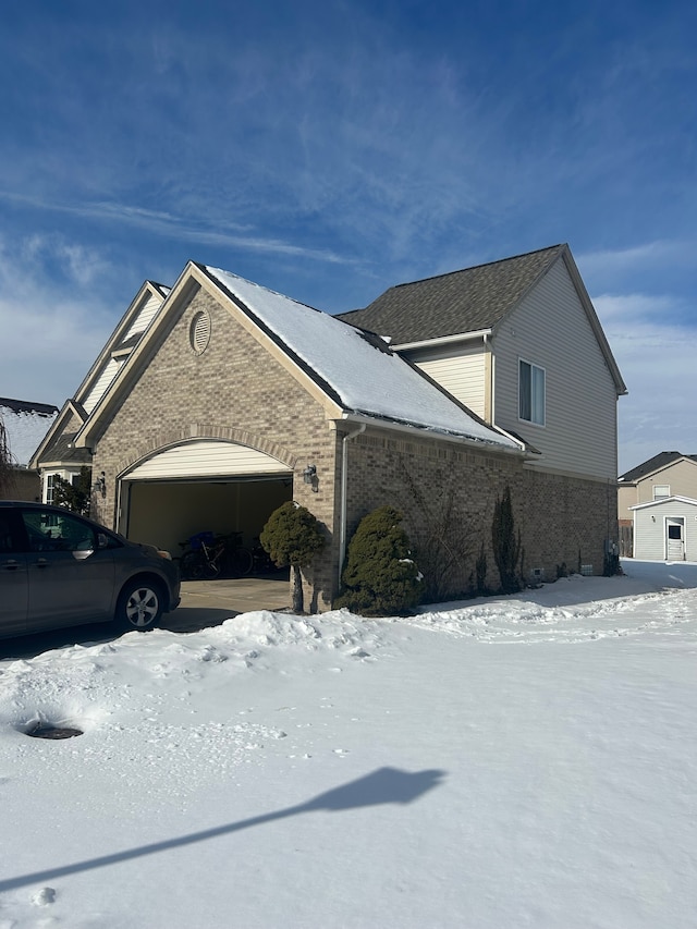 view of snowy exterior featuring a garage and brick siding