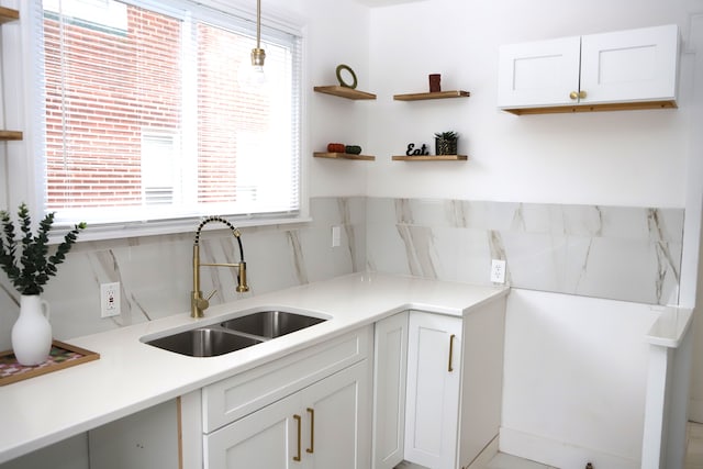 kitchen with light countertops, a sink, decorative light fixtures, and white cabinetry