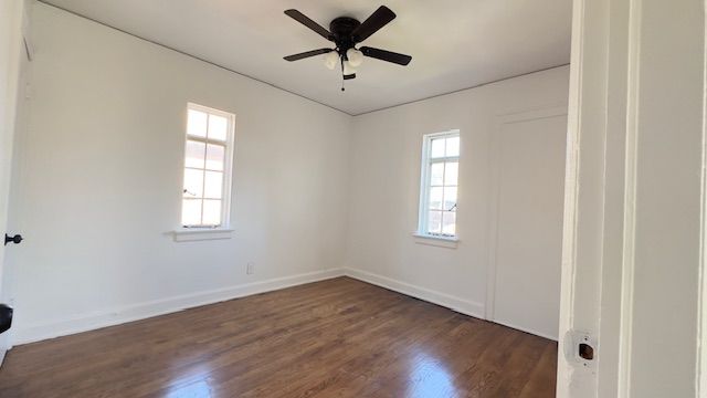 spare room with dark wood-type flooring, a ceiling fan, and baseboards