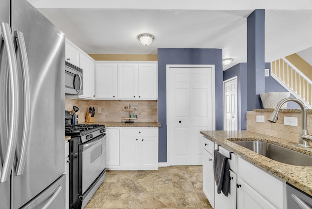 kitchen with white cabinetry, stainless steel appliances, light stone countertops, sink, and decorative backsplash