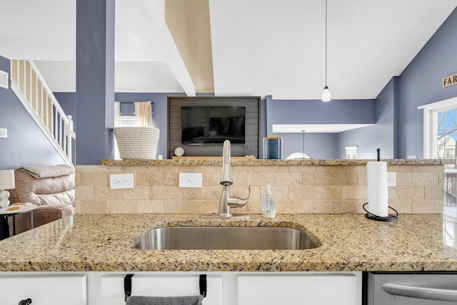 kitchen featuring light stone countertops, sink, white cabinets, decorative backsplash, and pendant lighting