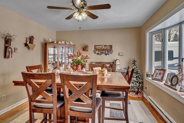 dining room with a baseboard heating unit, baseboards, a ceiling fan, and light wood-style floors