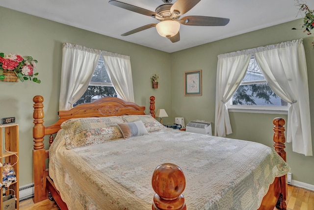 bedroom featuring a baseboard heating unit, ceiling fan, multiple windows, and light wood-style flooring