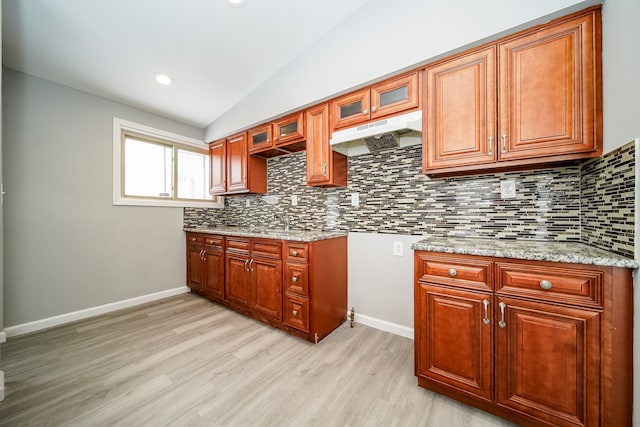 kitchen with light hardwood / wood-style flooring, sink, vaulted ceiling, light stone counters, and decorative backsplash