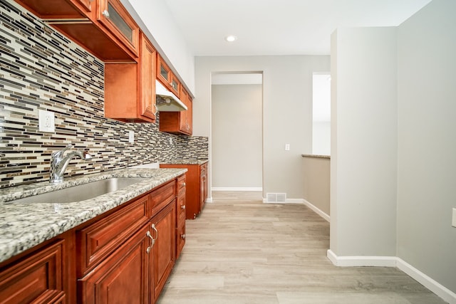 kitchen with sink, light stone counters, tasteful backsplash, and light hardwood / wood-style floors