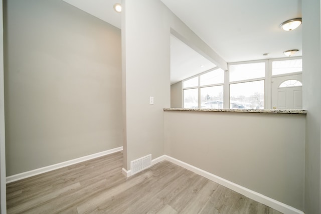 empty room featuring plenty of natural light, light wood-type flooring, and vaulted ceiling with beams