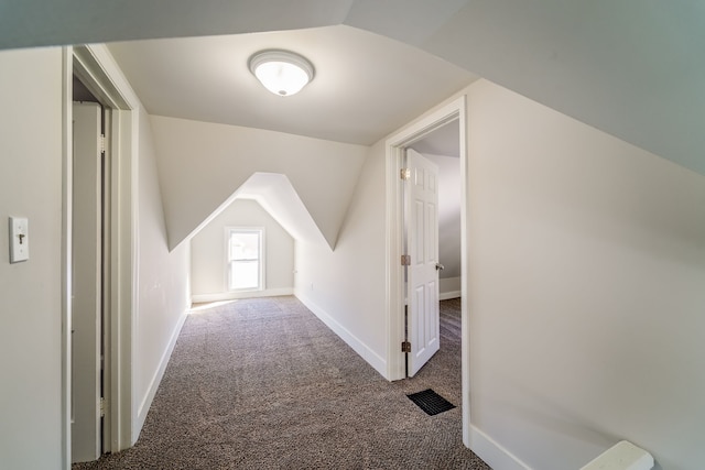 additional living space featuring lofted ceiling, dark carpet, visible vents, and baseboards