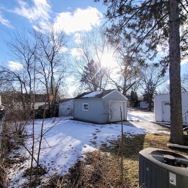 yard covered in snow with central AC unit, a shed, and a garage