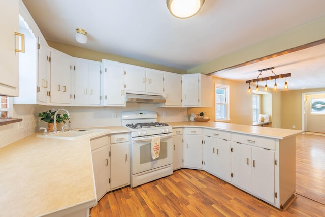 kitchen with hanging light fixtures, gas range gas stove, white cabinets, sink, and kitchen peninsula