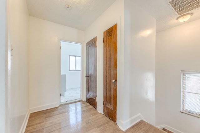 hallway featuring light wood-type flooring and a textured ceiling