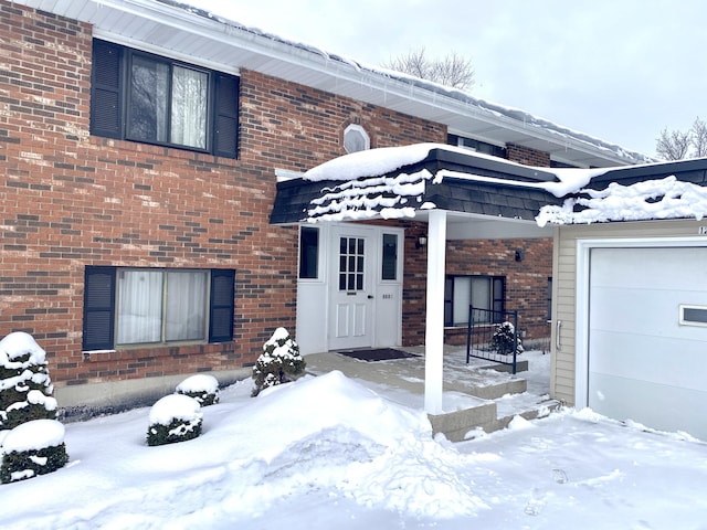 snow covered property entrance featuring brick siding