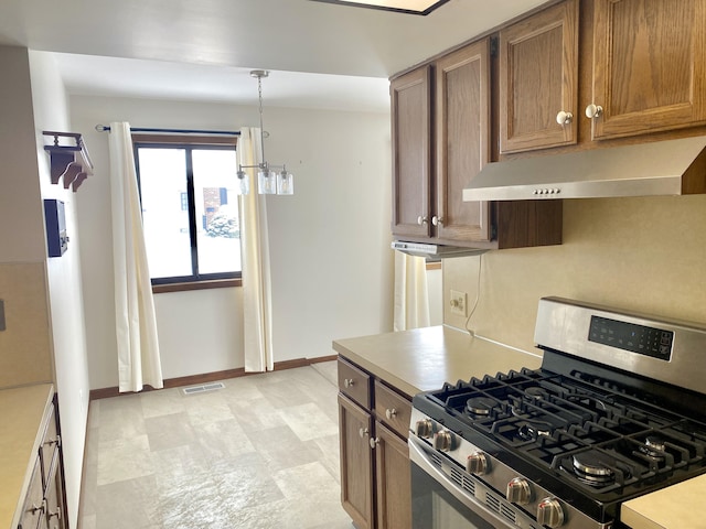 kitchen with stainless steel gas range oven, light countertops, under cabinet range hood, decorative light fixtures, and brown cabinetry