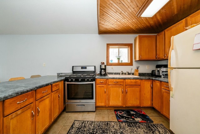 kitchen featuring freestanding refrigerator, dark countertops, stainless steel gas range oven, and a sink